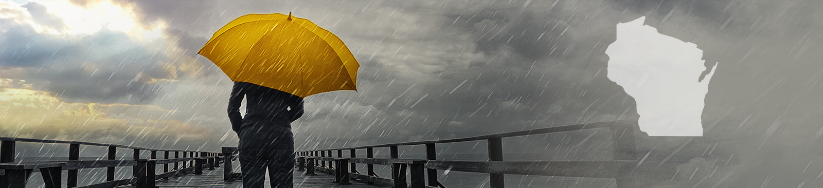 A person stands with their back to the camera, carrying a bright yellow umbrella in the middle of a storm. They stand on a pier, looking out at the stormy sky, which simultaneously looks threatening and hopeful as some of the clouds part to reveal a glimpse of sunshine.