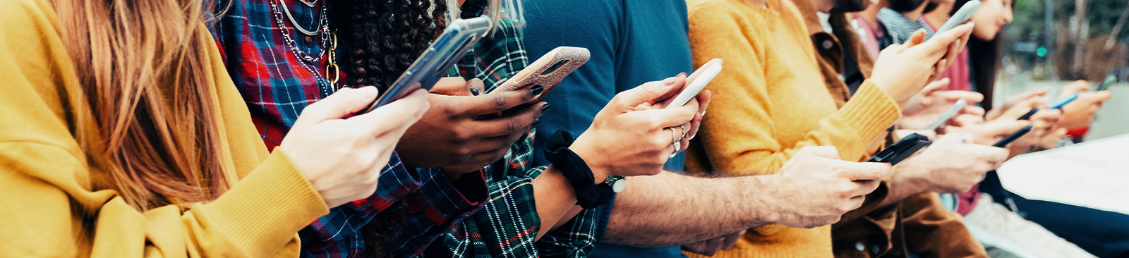 A diverse group of young adults sits on an outdoor platform, each person engaging with their phone.